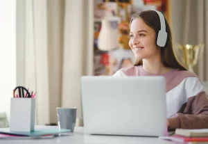 young-female-student-sitting-table-using-laptop-studying-happy-college-home-headphones-179896471